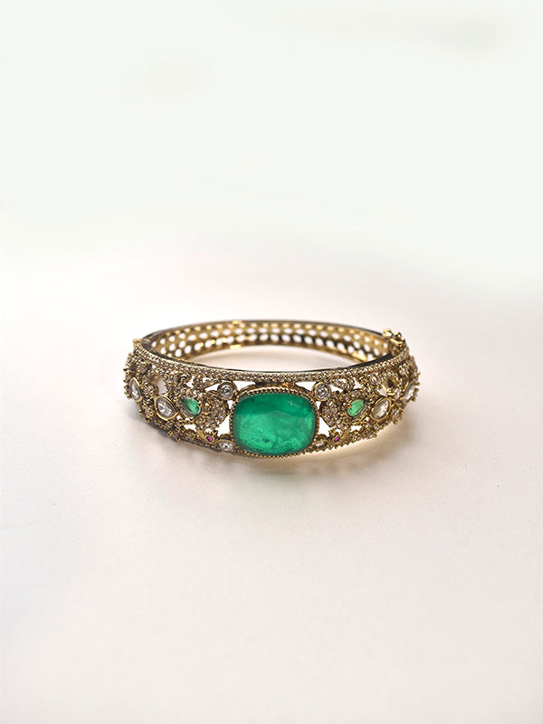 Gold bracelet with a green gemstone on a white background