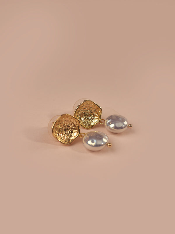  stud earrings with three silver toned oval stud earrings, arranged on a solid warm beige background